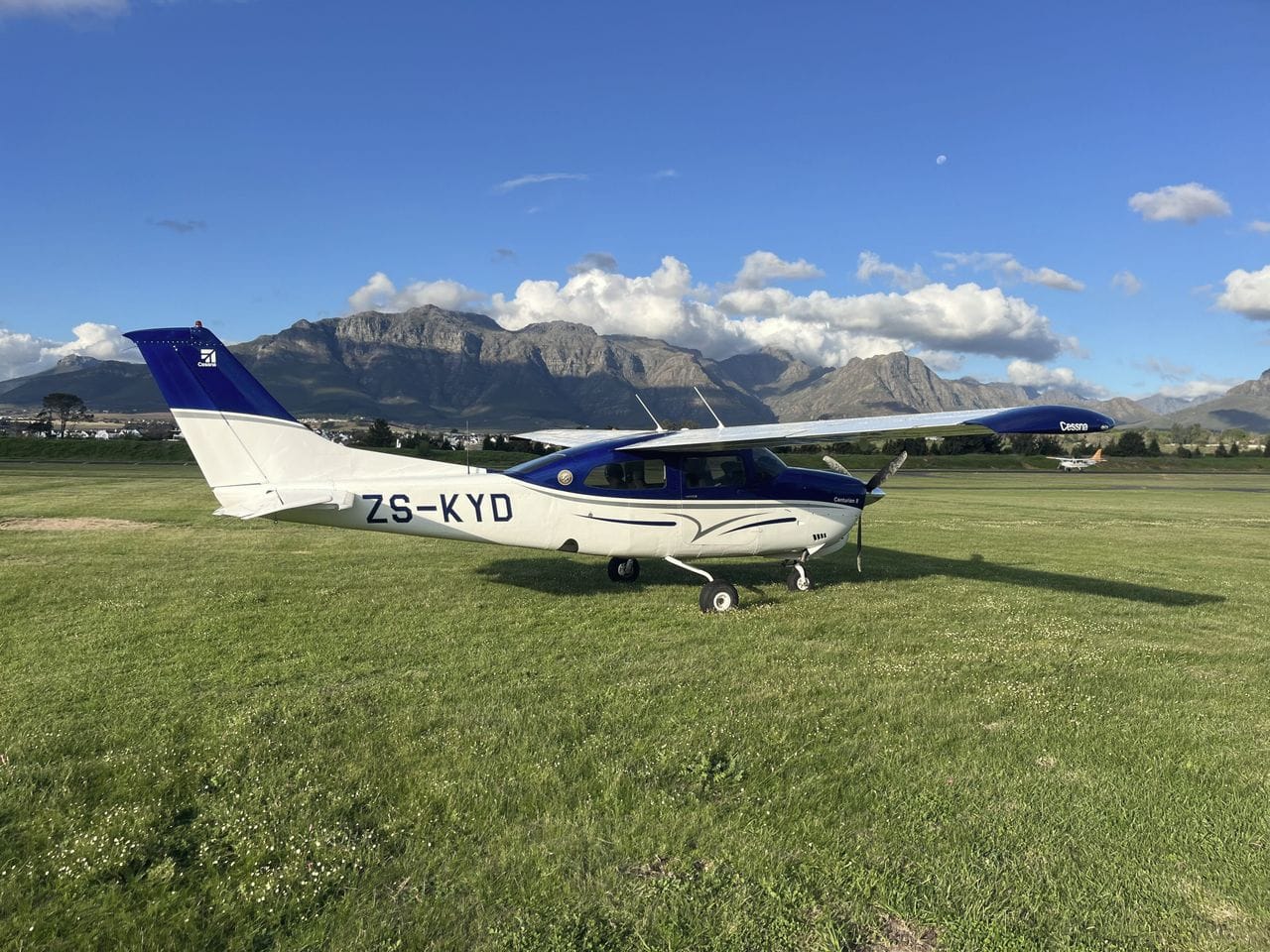 CIVAIR’s Cessna 210 Centurion II ZS-KYD parked on grass, the Stellenbosch mountains behind